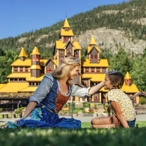 Prinsesse og barn med kroner foran Eventyrslottet i Hunderfossen Eventyrpark – en magisk opplevelse for små og store